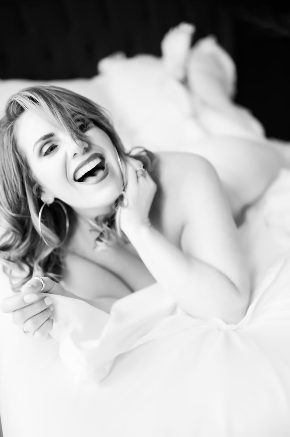 Playful photo of woman in her 40s laughing in-the-sheets, during self-discovery boudoir session with Betsy McCue Pictures.