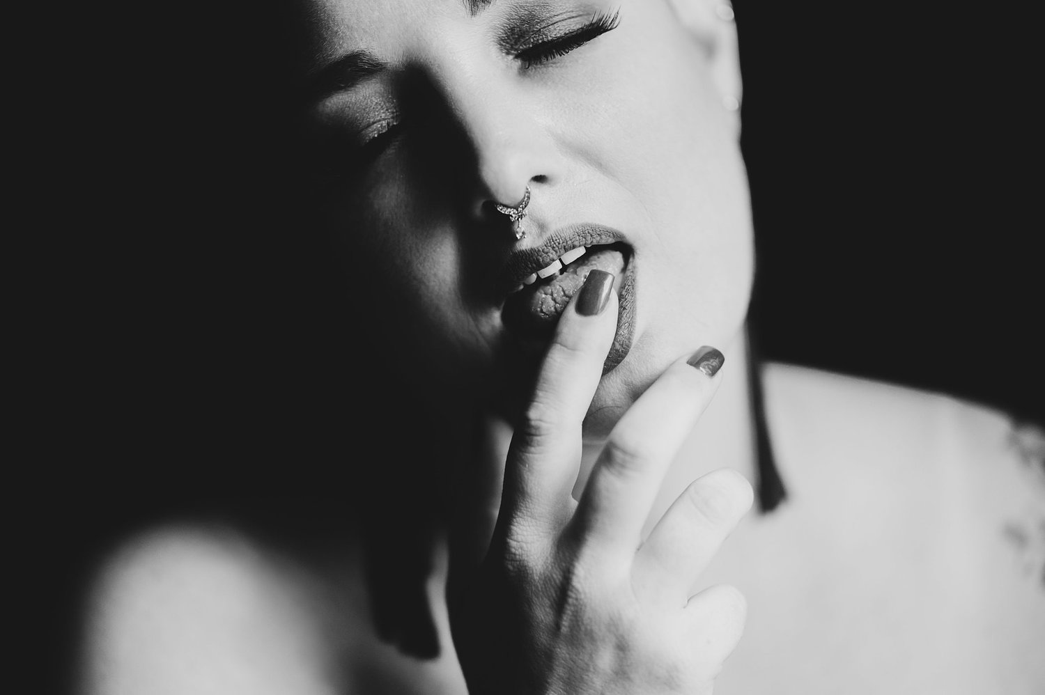 Erotic photo of woman touching her finger to her tongue, photographed in black-and-white.