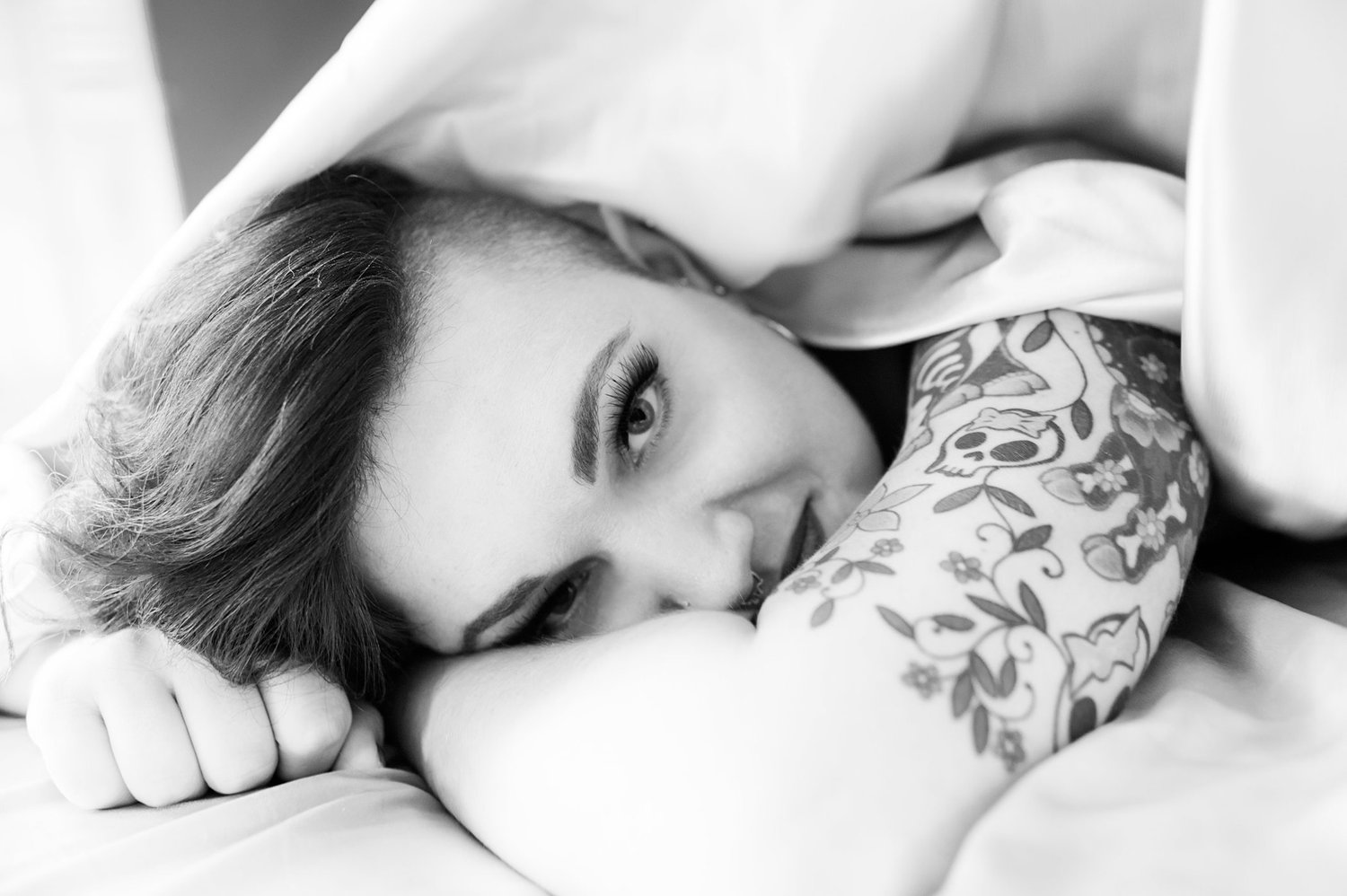 Black-and-white portrait of woman smiling at the camera lying on a bed.