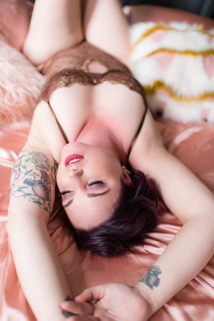 Emotive photo of woman in lace lingerie lying-in-the-sheets with her arms above her head.