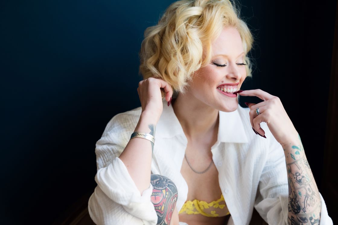 Woman wearing an opened white long sleeves that exposes her yellow lacy bra as she poses while biting her dark red nail