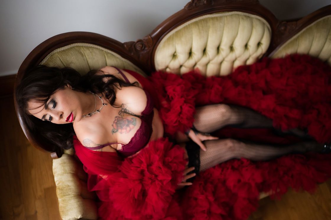 Woman wearing red lingerie with a red ruffled cover up while posing for a boudoir shot in a couch