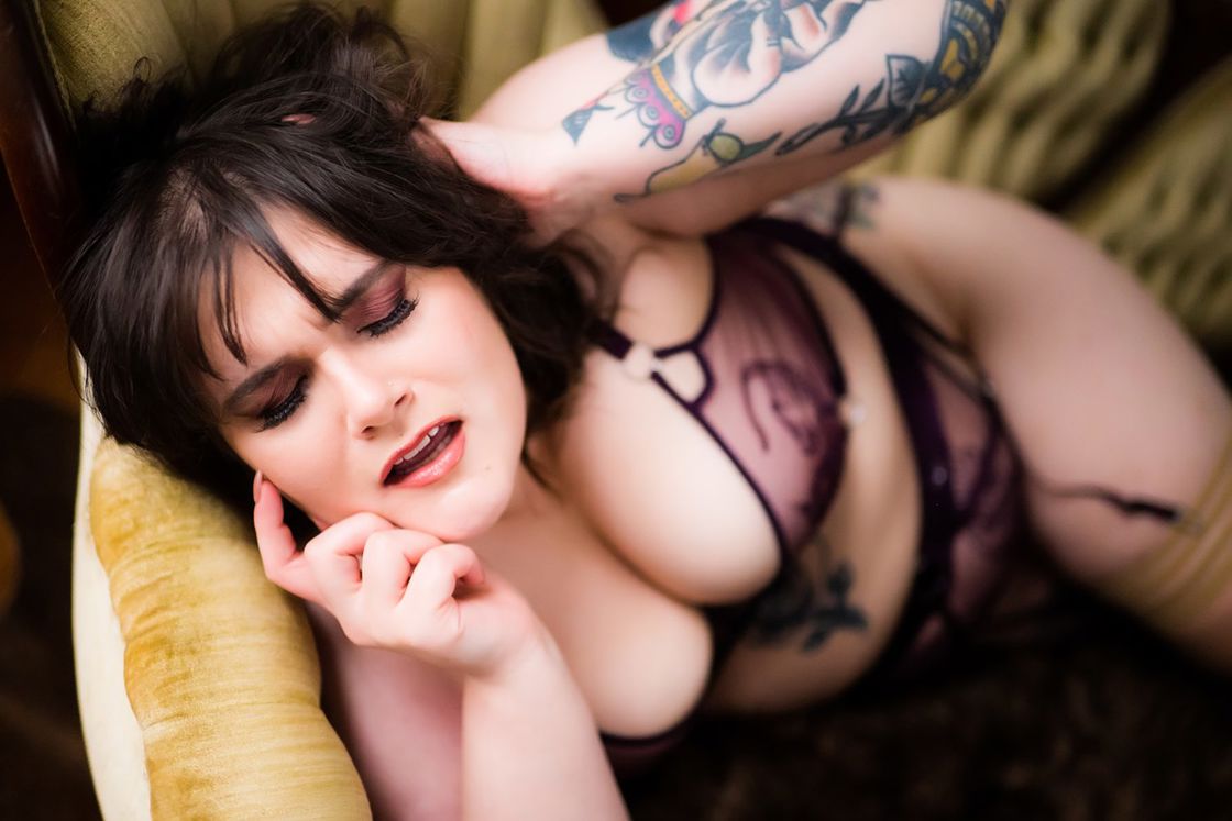 Woman wearing lacy purple, see through lingerie while posing for a boudoir shot in a couch