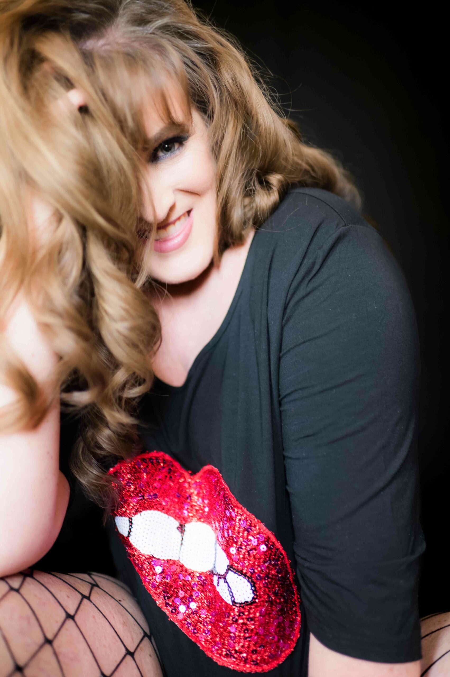 Photo of a woman, smiling at the camera, wearing a black shirt with big red lips print.