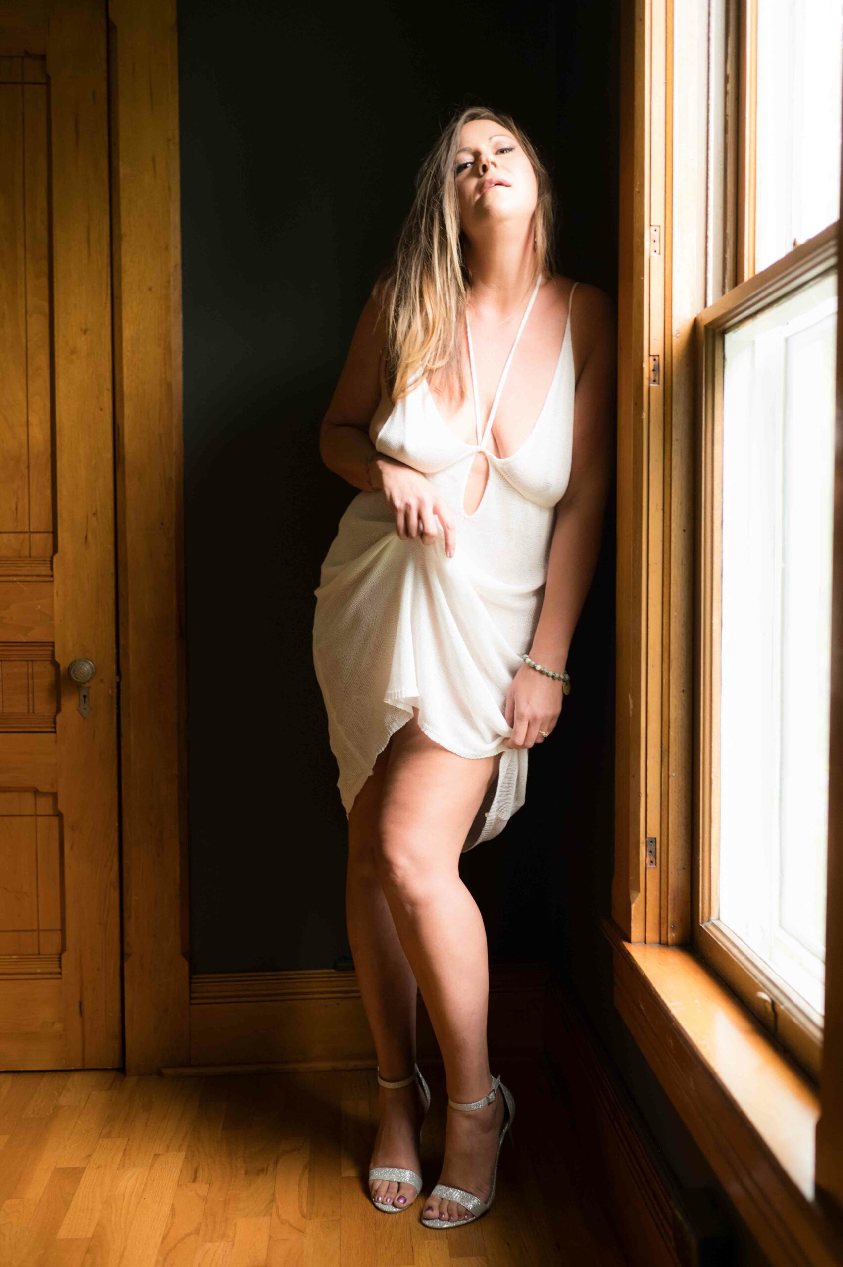 Photo of a woman standing beside a window, wearing white lingerie