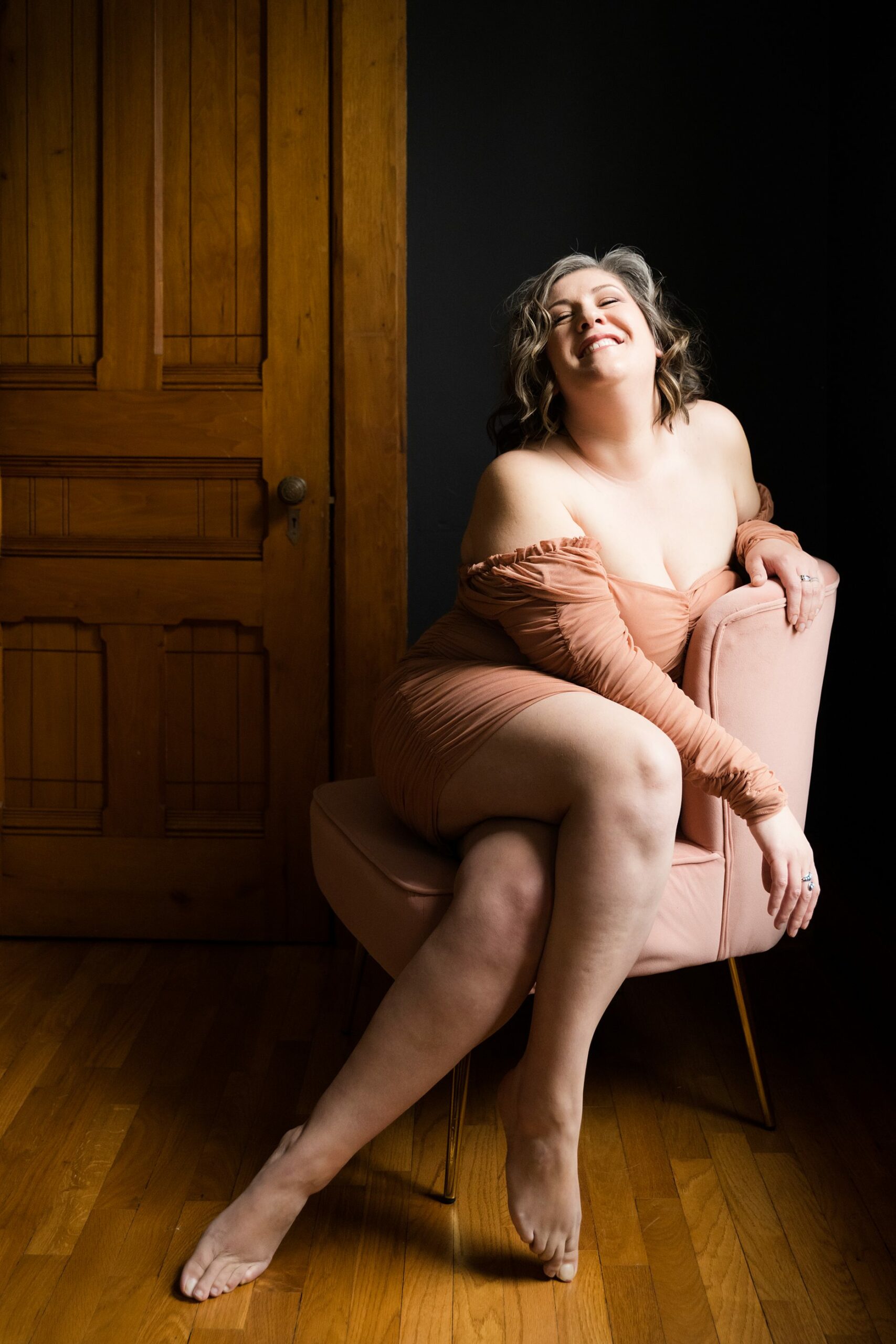 Lansing boudoir photo with women posing for beauty in a pink dress laughing