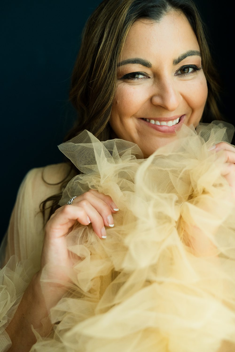 Close up boudoir portrait of woman wearing tan tulle robe smiling at the camera.