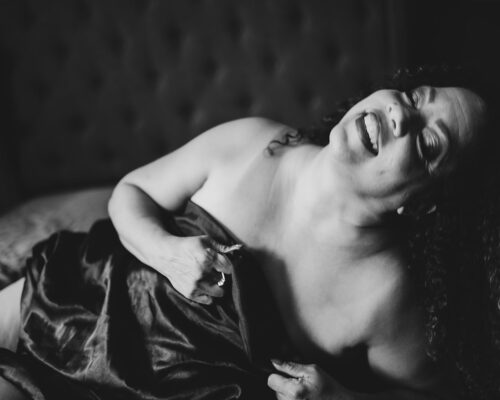 Romantic black-and-white-photo of woman smiling covering herself with a satin sheet.